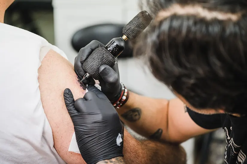 Best tattoo removal Perth – close-up of tattoo artist applying ink to a man's arm at a Perth grooming clinic